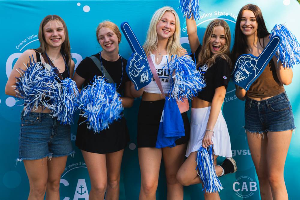 students posing in front of CAB backdrop at Laker Kickoff photo booth and holding pom poms